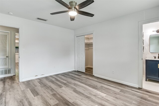 unfurnished bedroom with baseboards, visible vents, wood finished floors, and connected bathroom