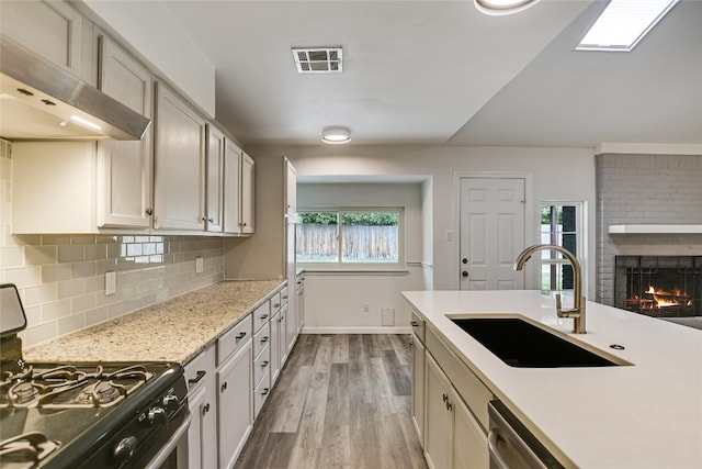 kitchen featuring visible vents, exhaust hood, a sink, light wood-type flooring, and stainless steel range with gas cooktop