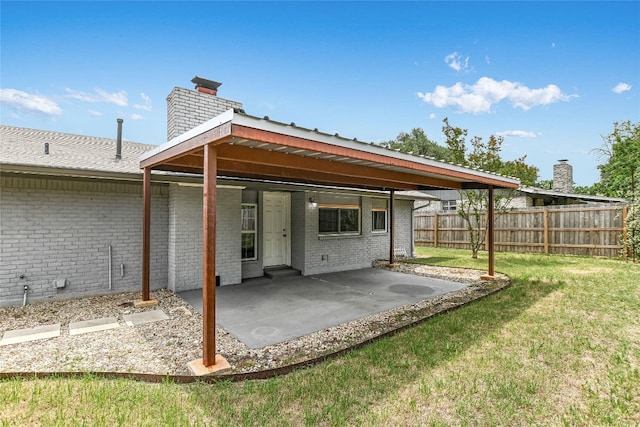 rear view of house featuring a chimney, a yard, brick siding, fence, and a patio area