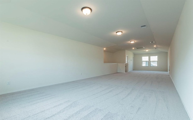 spare room with visible vents, vaulted ceiling, light carpet, and baseboards