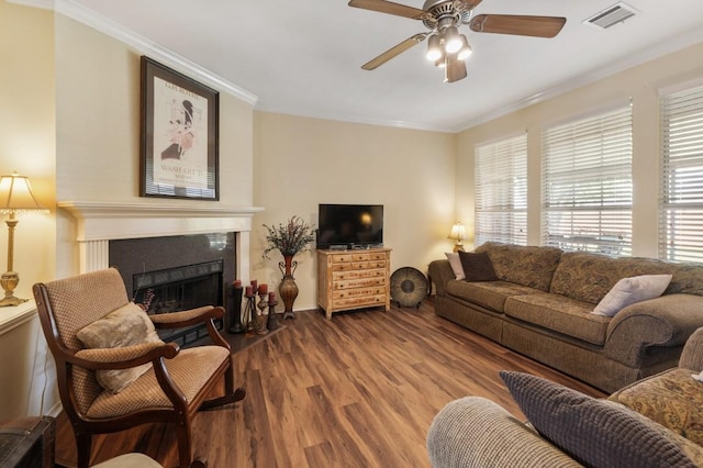 living room featuring a fireplace with flush hearth, ceiling fan, crown molding, visible vents, and wood finished floors