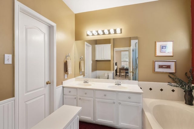 bathroom with a garden tub, double vanity, a sink, and wainscoting