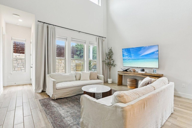 living room featuring baseboards, a healthy amount of sunlight, light wood-style floors, and a high ceiling