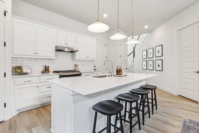 kitchen featuring recessed lighting, light wood finished floors, a sink, stainless steel gas range, and a kitchen breakfast bar