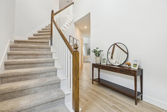 stairs with baseboards, wood finished floors, and a high ceiling