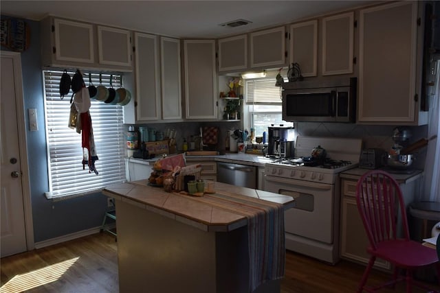 1200 NE 5th St, Smithville, TX 78957 - kitchen featuring stainless steel microwave, tile counters, white gas range, dishwasher, and a center island