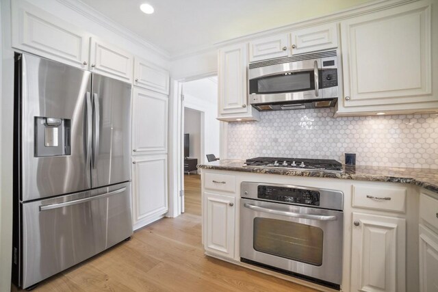 1702 Crested Butte Dr, Austin, TX 78746 - kitchen featuring stainless steel appliances, light wood finished floors, dark stone counters, backsplash, and white cabinetry