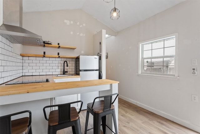 kitchen with a sink, wood counters, black electric stovetop, and wall chimney range hood