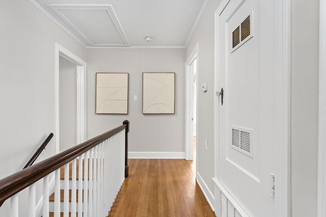 hallway with ornamental molding, visible vents, baseboards, and light wood-style floors