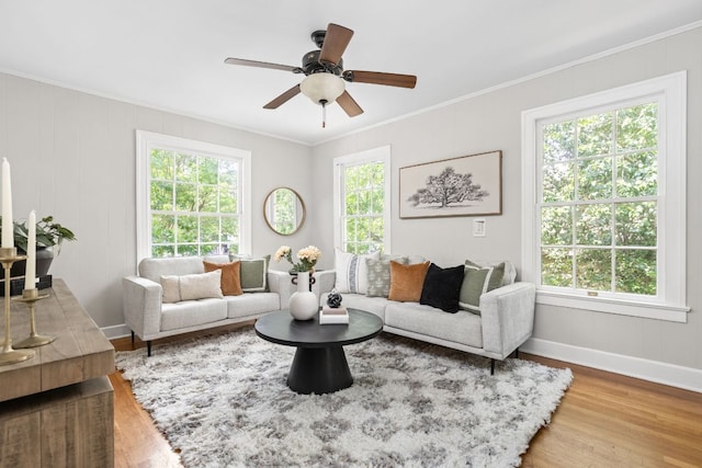 living area with baseboards, ornamental molding, a ceiling fan, and wood finished floors