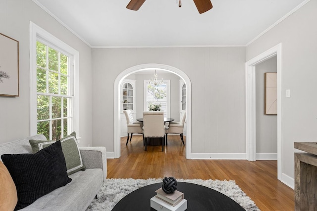 living room with arched walkways, ceiling fan with notable chandelier, wood finished floors, and crown molding