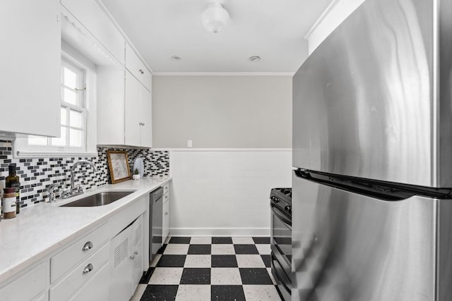kitchen featuring a sink, stainless steel appliances, a wainscoted wall, dark floors, and white cabinetry