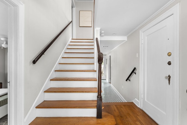 stairs featuring wood finished floors, crown molding, and baseboards
