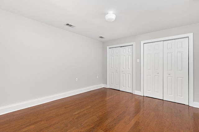 unfurnished bedroom with visible vents, baseboards, multiple closets, and dark wood finished floors