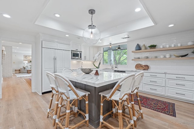 129 The Hills Dr, The Hills, TX 78738 - kitchen with a raised ceiling, white cabinetry, tasteful backsplash, a kitchen breakfast bar, and recessed lighting