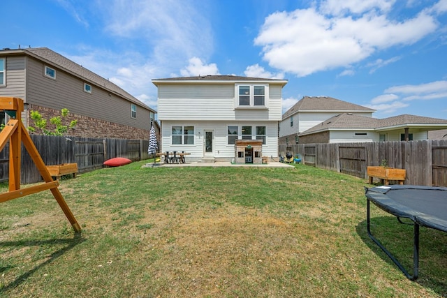 back of house featuring a trampoline, a fenced backyard, a yard, and a patio area