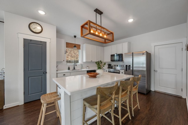 kitchen featuring a breakfast bar, appliances with stainless steel finishes, light countertops, a sink, and dark wood-type flooring