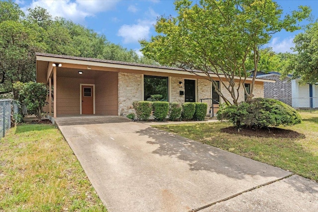 ranch-style house featuring a front lawn, an attached carport, stone siding, concrete driveway, and fence