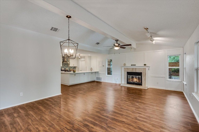 unfurnished living room featuring a tile fireplace, vaulted ceiling with beams, visible vents, wood finished floors, and ceiling fan with notable chandelier