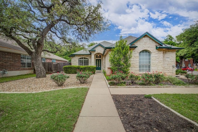 french country style house with fence, a front lawn, and stone siding