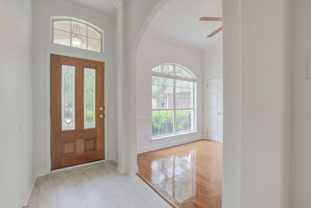 entrance foyer featuring baseboards, ornamental molding, a ceiling fan, and arched walkways