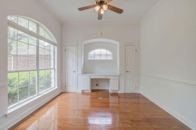 empty room featuring light wood-style floors, ceiling fan, ornamental molding, and built in study area