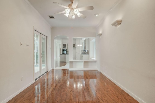 unfurnished living room featuring wood finished floors, arched walkways, ornamental molding, visible vents, and a ceiling fan