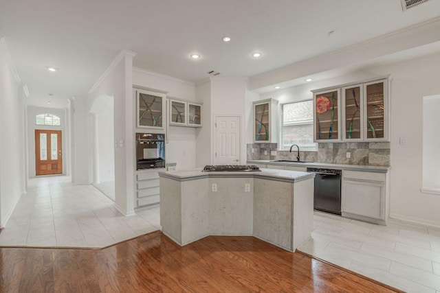 kitchen with decorative backsplash, glass insert cabinets, crown molding, black appliances, and a kitchen island