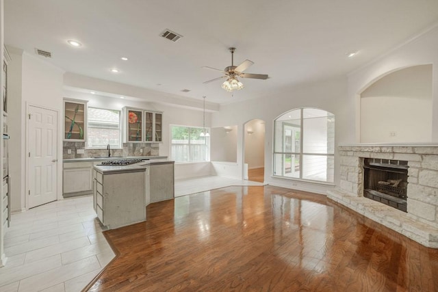 kitchen featuring a kitchen island, a stone fireplace, visible vents, a ceiling fan, and open floor plan