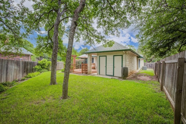 exterior space with an outdoor structure, a wooden deck, a shingled roof, a yard, and a fenced backyard