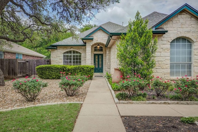 view of front of home with fence, roof with shingles, french doors, and stone siding