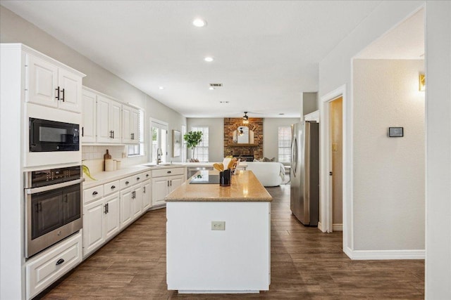 9007 Tweed Berwick Dr, Austin, TX 78750 - kitchen featuring appliances with stainless steel finishes, a kitchen island, open floor plan, white cabinetry, and dark wood finished floors