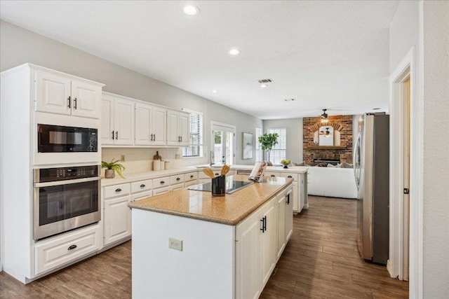 9007 Tweed Berwick Dr, Austin, TX 78750 - kitchen featuring a center island, a fireplace, black appliances, open floor plan, and white cabinetry