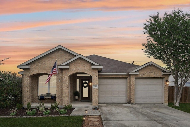 view of front of home featuring driveway, roof with shingles, fence, brick siding, and a garage