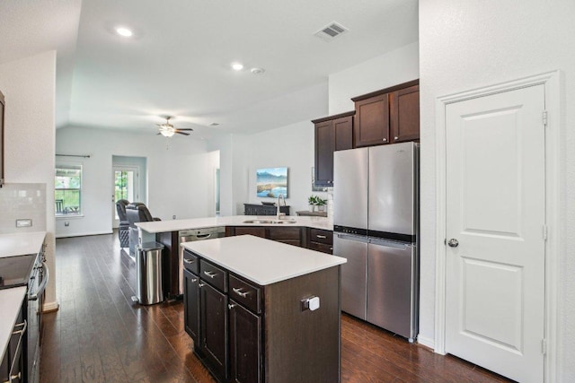 kitchen featuring appliances with stainless steel finishes, dark brown cabinets, a sink, dark wood-style floors, and a peninsula