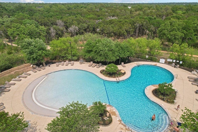 pool with a patio, a forest view, and fence