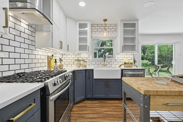 kitchen with white cabinets, a sink, wall chimney exhaust hood, gas range, and glass insert cabinets