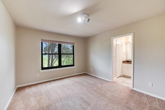 unfurnished bedroom with connected bathroom, light carpet, and baseboards