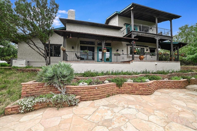 back of property with a chimney, a porch, a balcony, and stucco siding