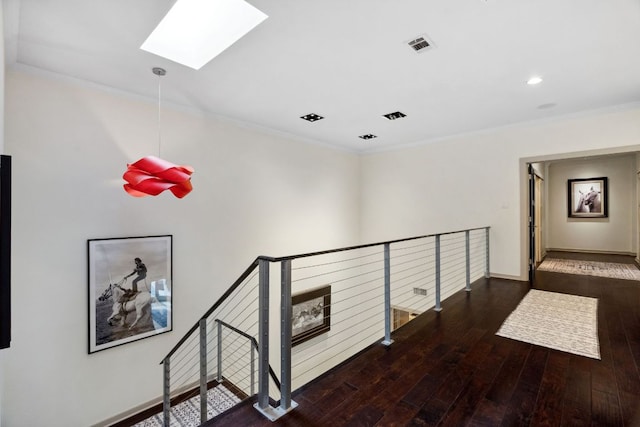 corridor with a skylight, hardwood / wood-style floors, ornamental molding, an upstairs landing, and baseboards