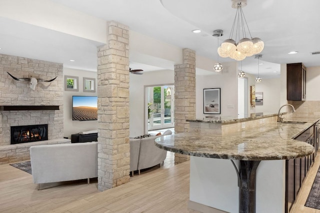9 Swiftwater Trl, The Hills, TX 78738 - kitchen with decorative columns, light stone countertops, light wood-style floors, a peninsula, and dark brown cabinets