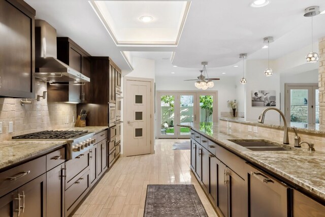 kitchen featuring tasteful backsplash, stainless steel appliances, dark brown cabinets, a sink, and wall chimney exhaust hood