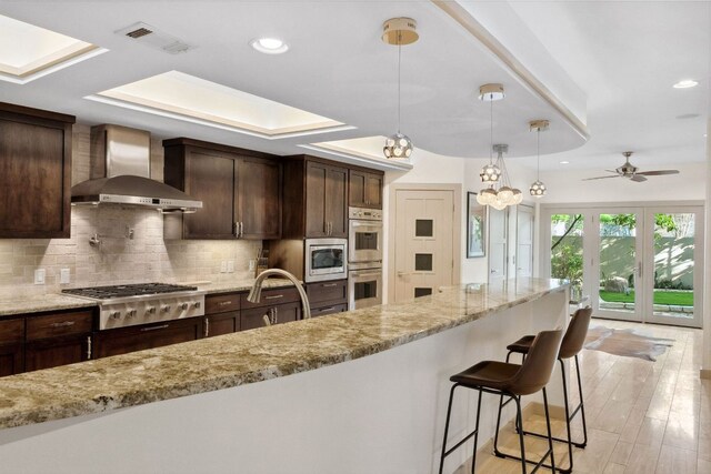 9 Swiftwater Trl, The Hills, TX 78738 - kitchen featuring wall chimney exhaust hood, appliances with stainless steel finishes, backsplash, light stone countertops, and recessed lighting
