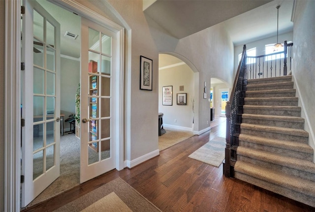 staircase with wood finished floors, visible vents, baseboards, arched walkways, and french doors