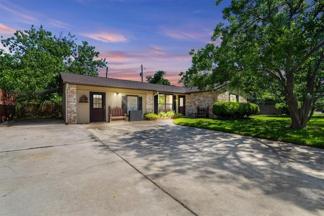 ranch-style home featuring a lawn, fence, driveway, and stone siding