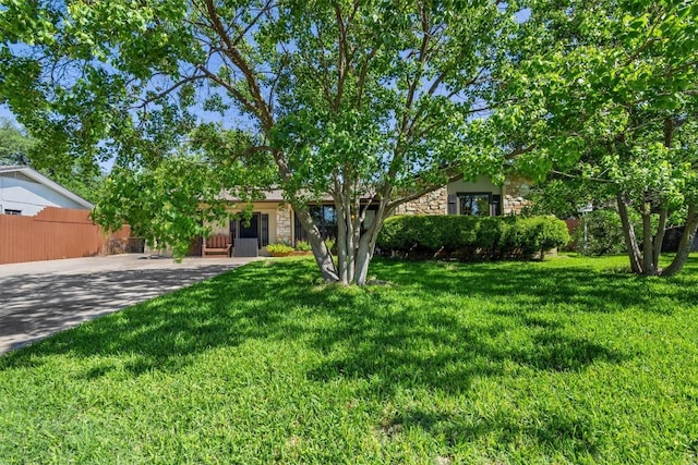 view of front of property with fence, driveway, a front lawn, and stone siding