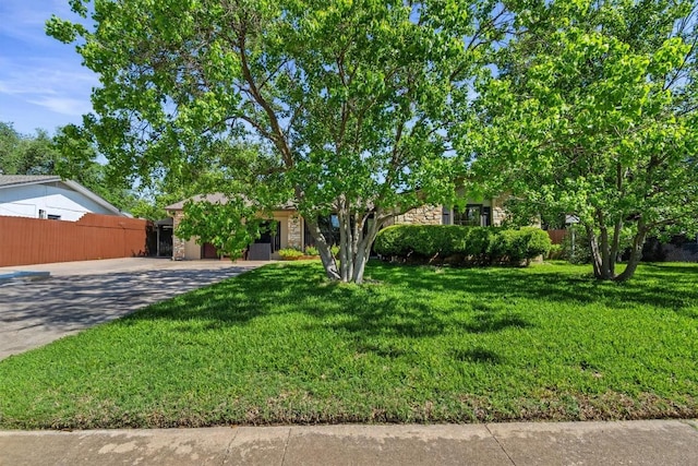 obstructed view of property featuring a front lawn, fence, stone siding, and concrete driveway