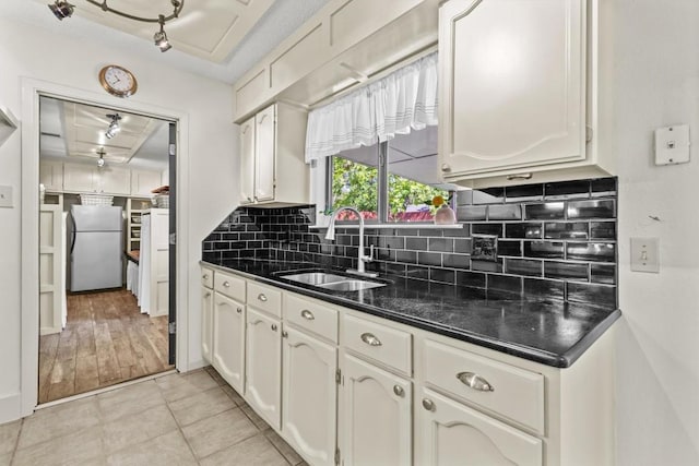 kitchen with white cabinets, dark countertops, a sink, freestanding refrigerator, and tasteful backsplash