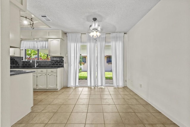 unfurnished dining area with a sink, a textured ceiling, baseboards, light tile patterned floors, and visible vents