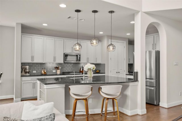 18617 Rio Chama Ln, Austin, TX 78738 - kitchen with appliances with stainless steel finishes, decorative backsplash, an island with sink, arched walkways, and dark wood-style floors